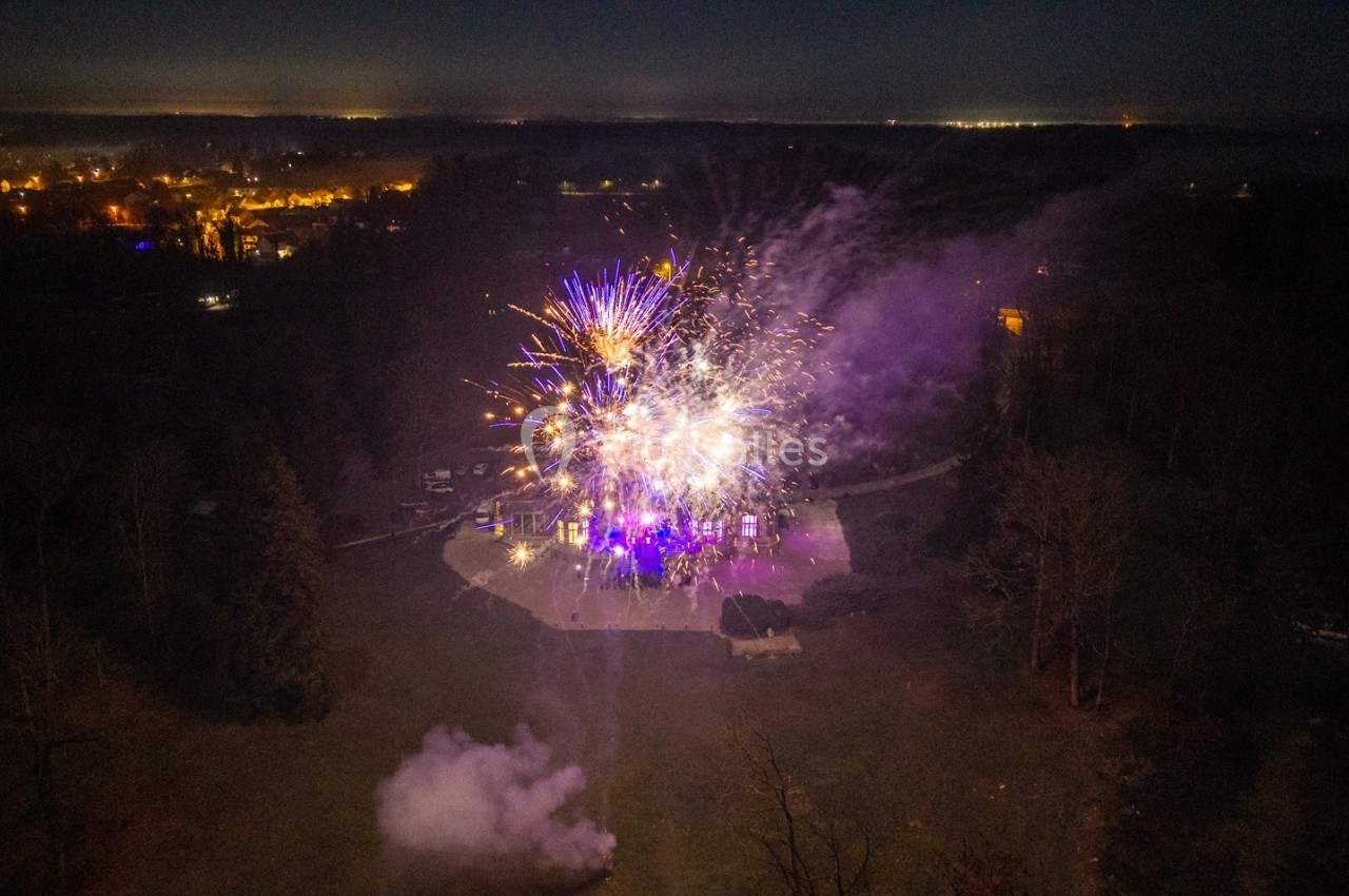 Feu d'artifice illuminant un parc la nuit, avec des éclats colorés et une ville visible en arrière-plan.