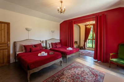 Chambre lumineuse avec lit double, meubles en bois sculpté, tapis décoratif et grande fenêtre avec rideaux.