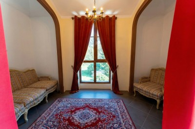 Chambre lumineuse avec lit double, meubles en bois sculpté, tapis décoratif et grande fenêtre avec rideaux.