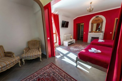 Chambre lumineuse avec lit double, meubles en bois sculpté, tapis décoratif et grande fenêtre avec rideaux.