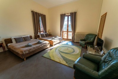 Chambre lumineuse avec lit double, meubles en bois sculpté, tapis décoratif et grande fenêtre avec rideaux.