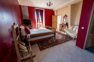Chambre lumineuse avec lit double, meubles en bois sculpté, tapis décoratif et grande fenêtre avec rideaux.