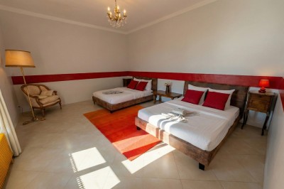 Chambre lumineuse avec lit double, meubles en bois sculpté, tapis décoratif et grande fenêtre avec rideaux.