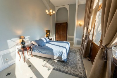 Chambre lumineuse avec lit double, meubles en bois sculpté, tapis décoratif et grande fenêtre avec rideaux.