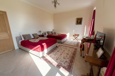 Chambre lumineuse avec lit double, meubles en bois sculpté, tapis décoratif et grande fenêtre avec rideaux.