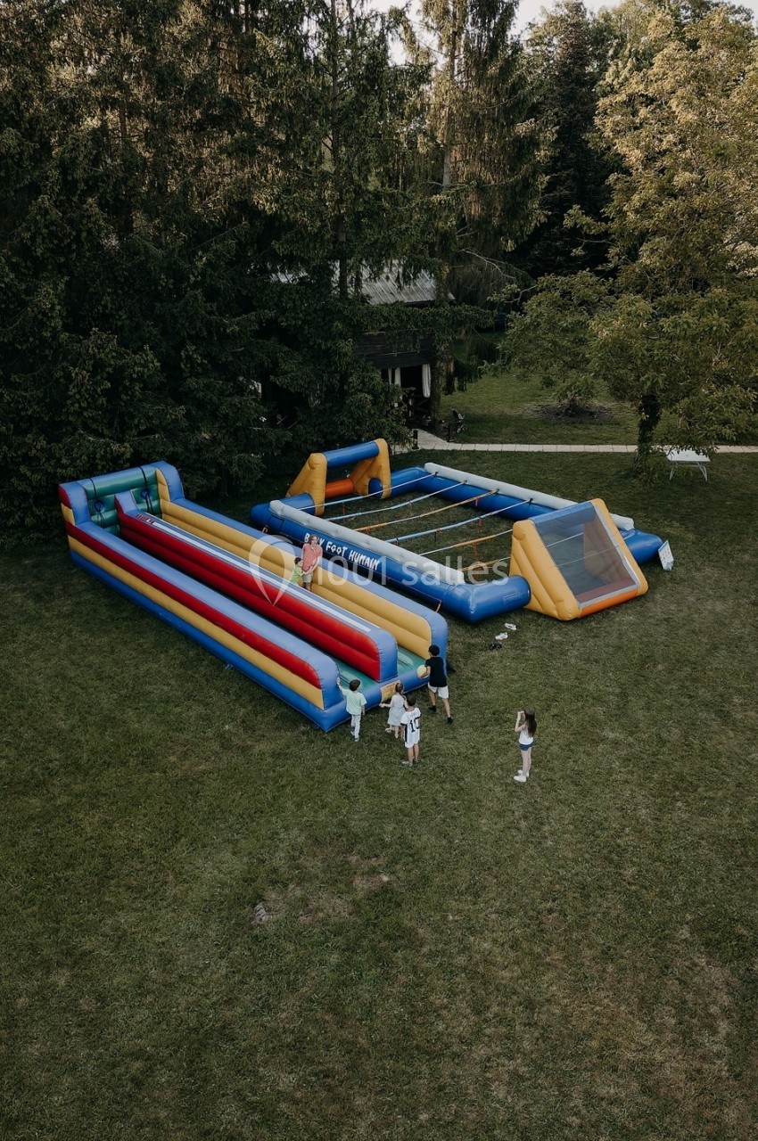 Structures gonflables colorées installées sur une pelouse, avec des enfants jouant autour et des arbres en arrière-plan.