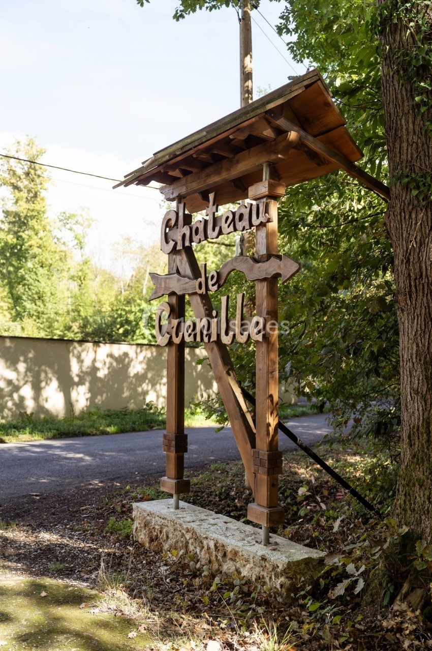 Panneau en bois indiquant ’Château de Glenille’, situé près d'une route bordée d'arbres.
