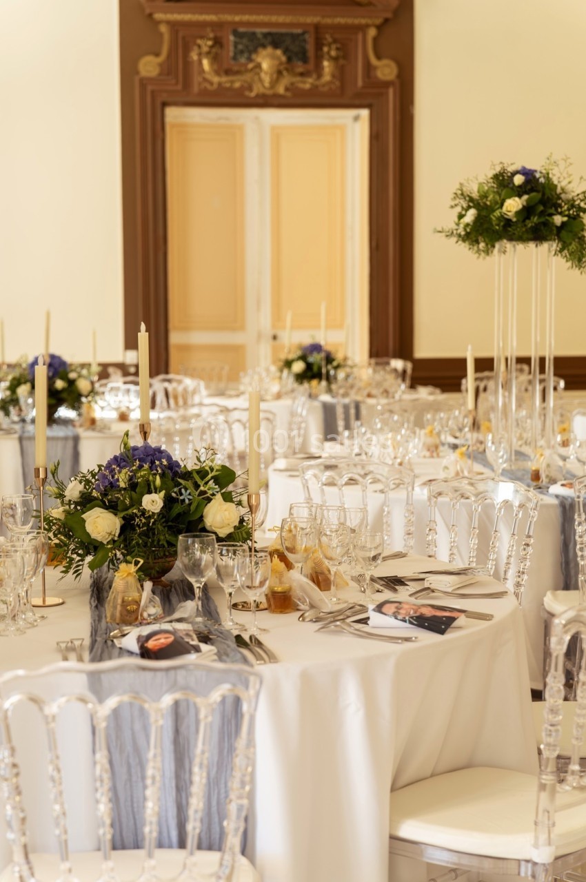 Salle de réception élégante avec tables rondes décorées de fleurs, bougies et vaisselle raffinée.