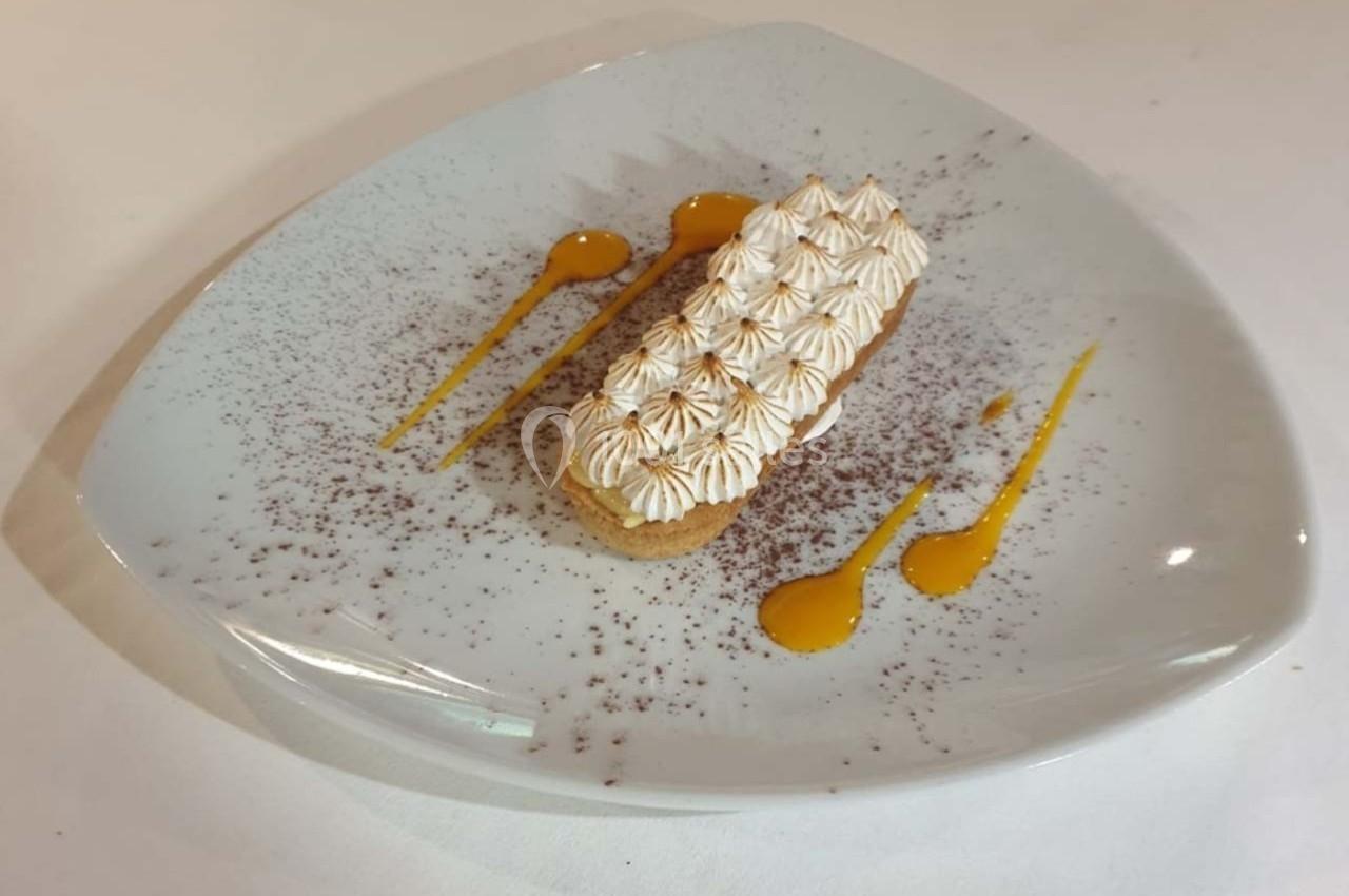 Tartelette meringuée sur assiette triangulaire, décorée de coulis jaune et de poudre de cacao.