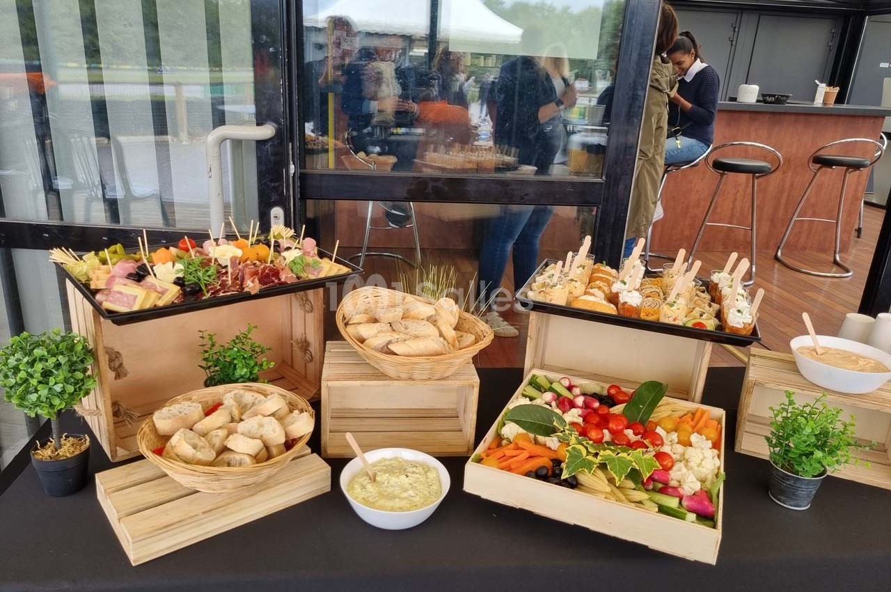 Buffet composé de pains, légumes frais, brochettes apéritives et sauces, présenté sur une table en extérieur couvert.