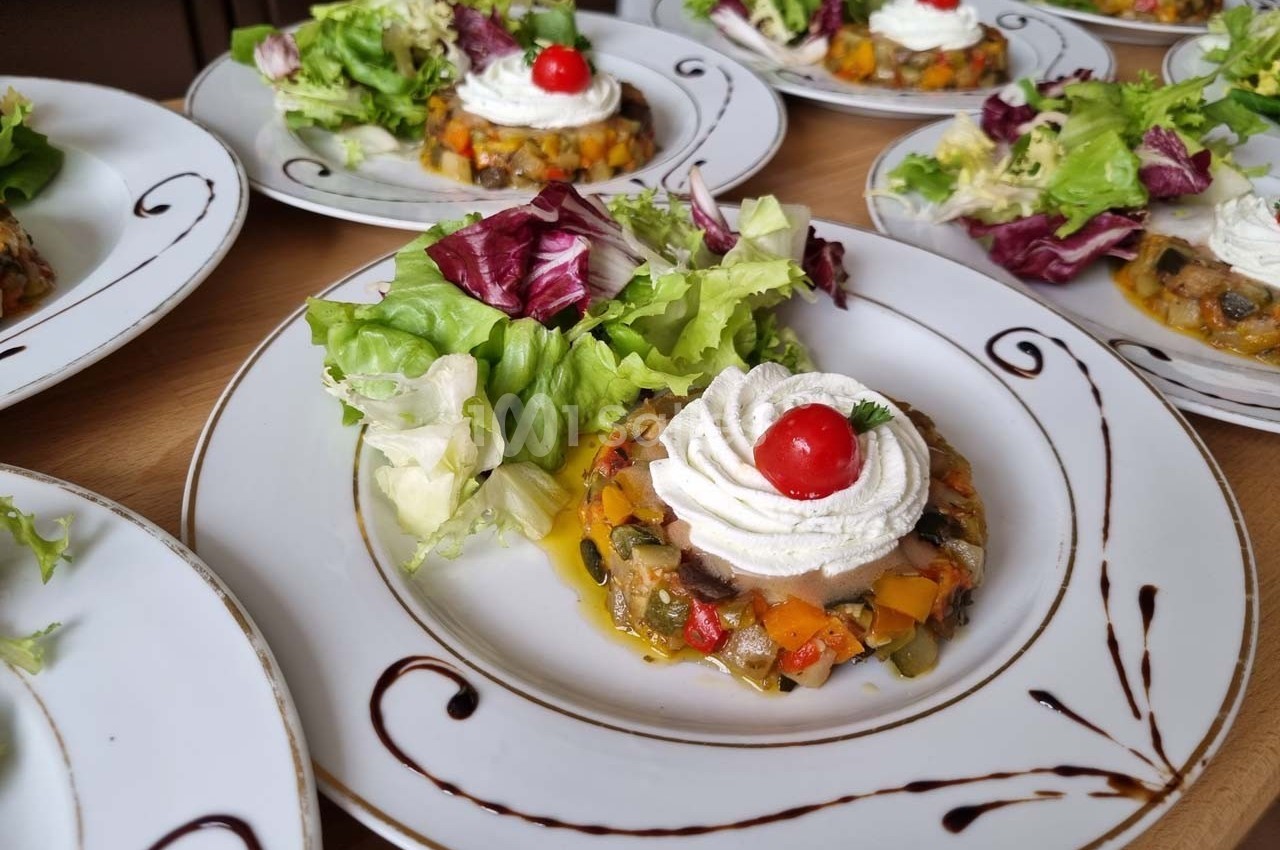 Assiette dressée avec une ratatouille en cercle, surmontée de chantilly salée et d'une tomate cerise, accompagnée de salade…