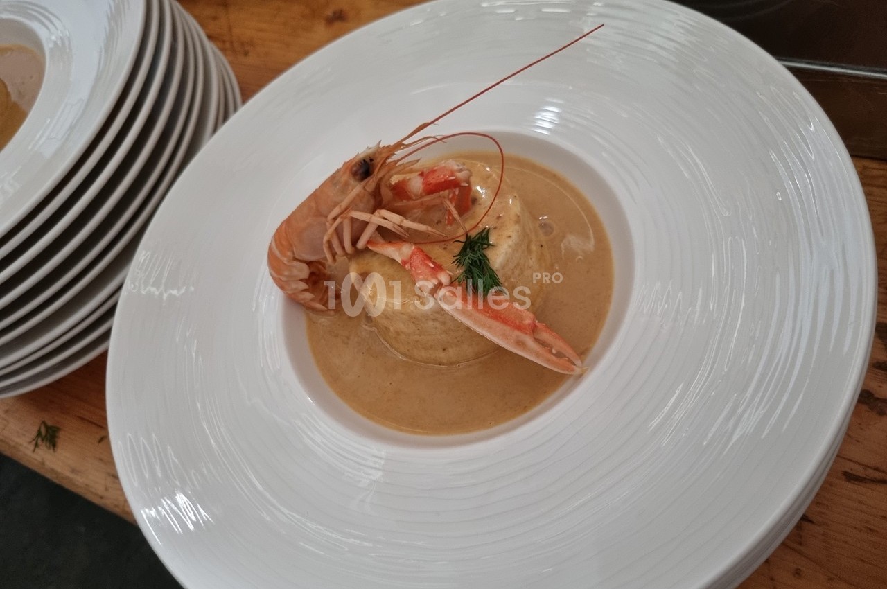 Assiette de bisque de crustacés avec une quenelle et une langoustine, servie sur une table en bois.