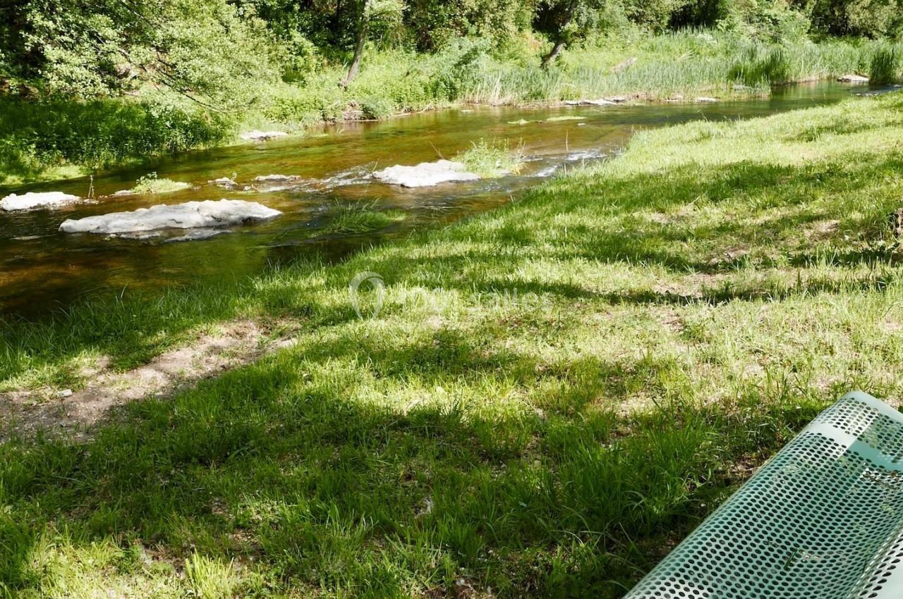 Banc en métal vert installé près d'une rivière entourée de végétation et d'arbres sous un ciel dégagé.