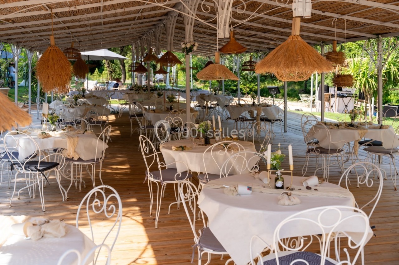 Terrasse couverte d'un restaurant avec des tables dressées, chaises en fer forgé et décorations en osier.