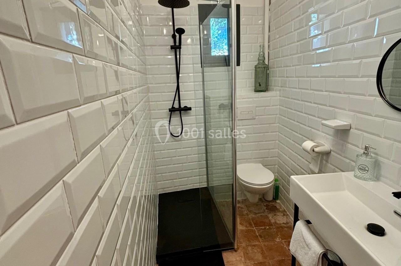 Salle de bain étroite avec douche à l'italienne, carrelage blanc, sol en terre cuite et lavabo avec miroir rond.