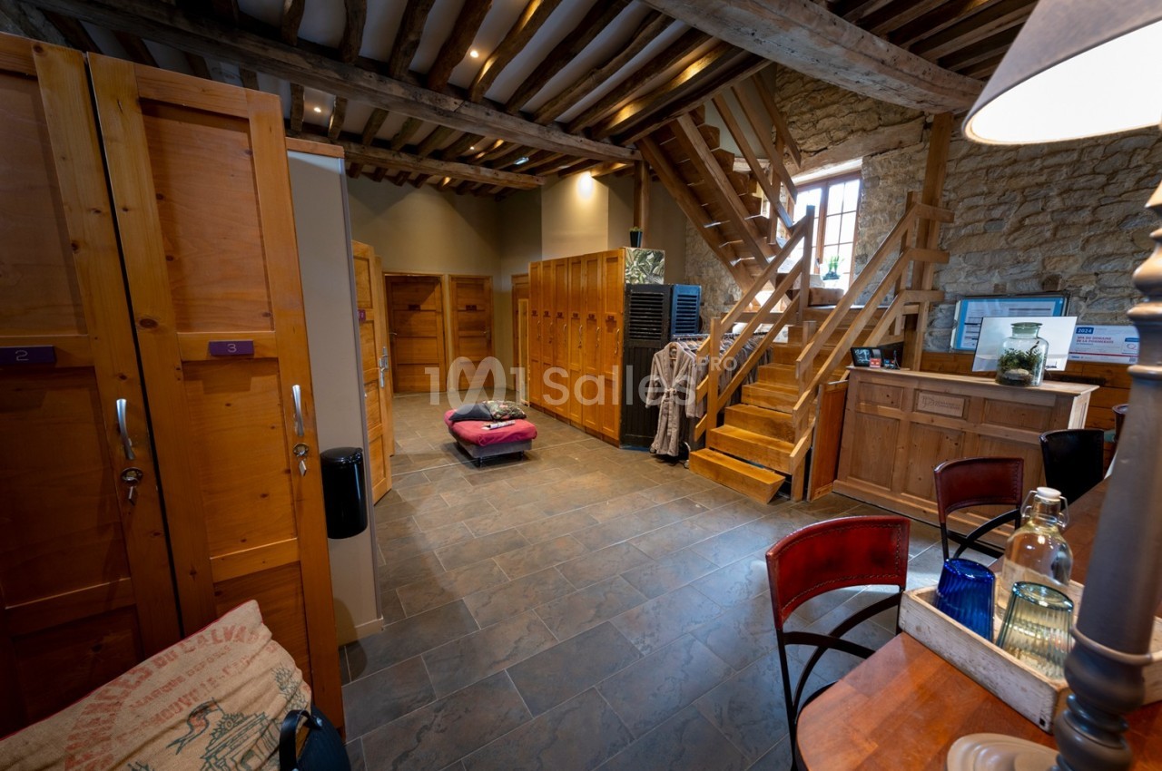 Vestiaire en bois avec casiers, banc central, escalier en bois et murs en pierre dans un espace chaleureux.