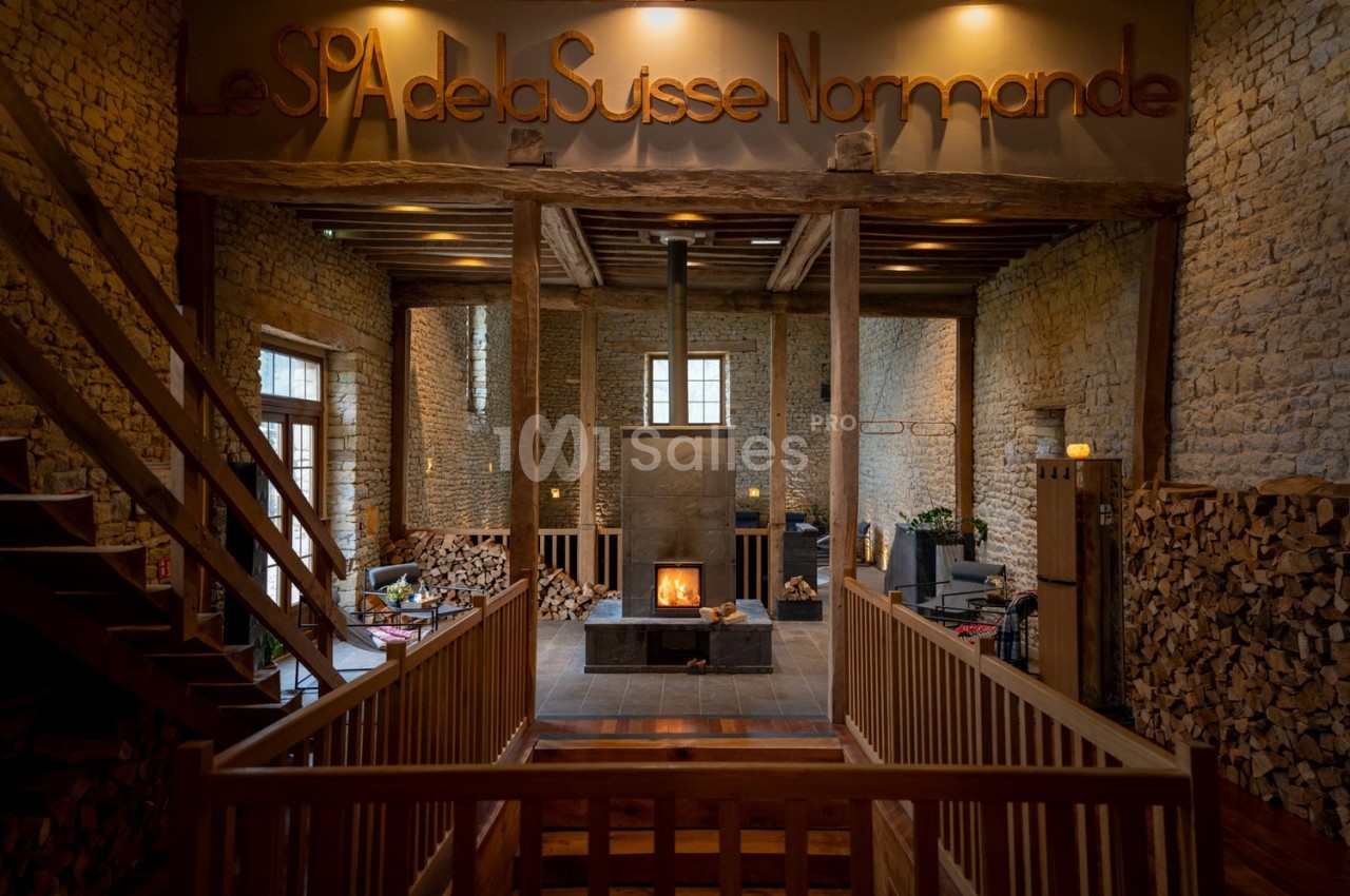 Intérieur d'un spa avec murs en pierre, cheminée centrale allumée et ambiance chaleureuse.