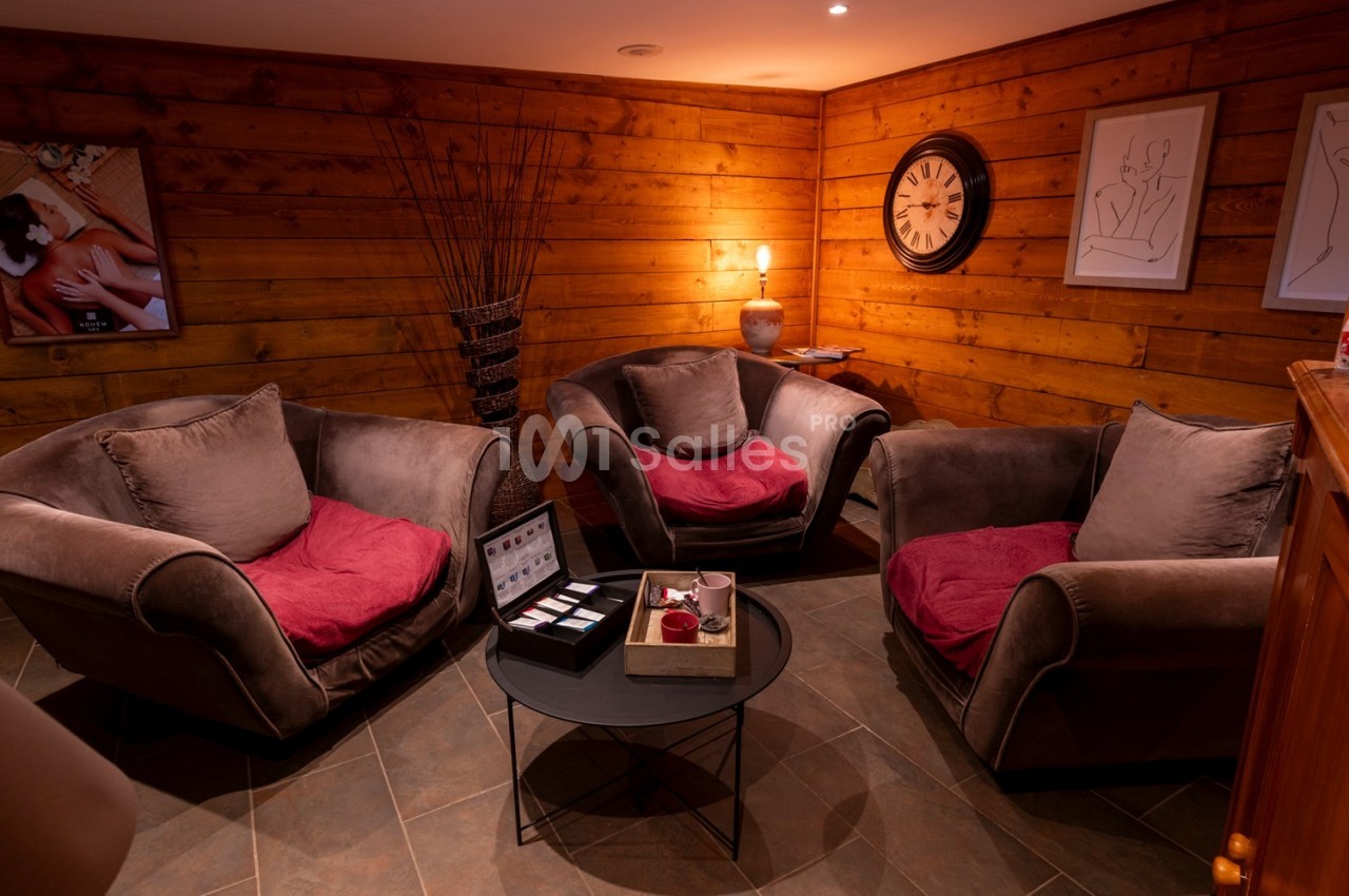 Salon chaleureux avec murs en bois, trois fauteuils autour d'une table basse et décorations murales.