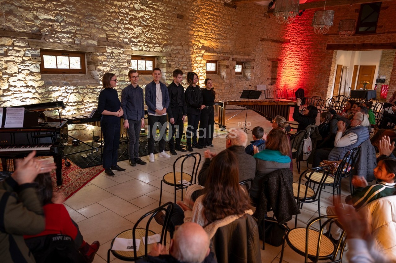 Un groupe de musiciens saluant un public dans une salle en pierre avec des instruments visibles en arrière-plan.