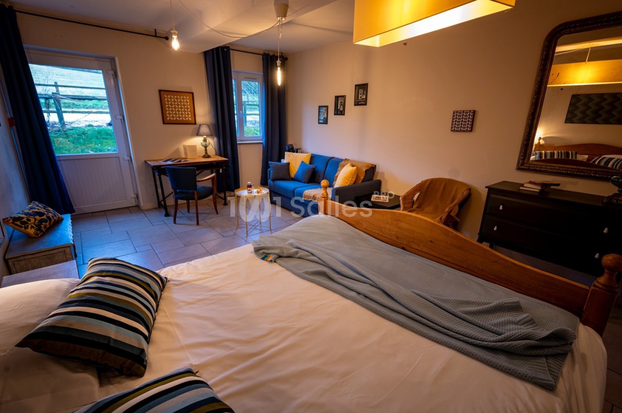 Chambre lumineuse avec lit double, coin salon, bureau, miroir mural et vue sur l'extérieur par une porte-fenêtre.