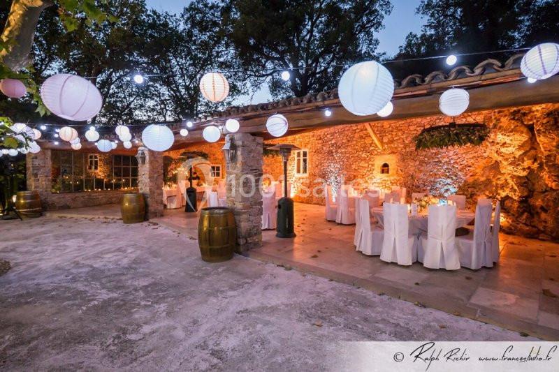 Location salle Signes (Var) - Château de Cancerilles #21 Salle extérieure en pierre éclairée par des guirlandes lumineuses et décorée de lanternes et de tables dressées.