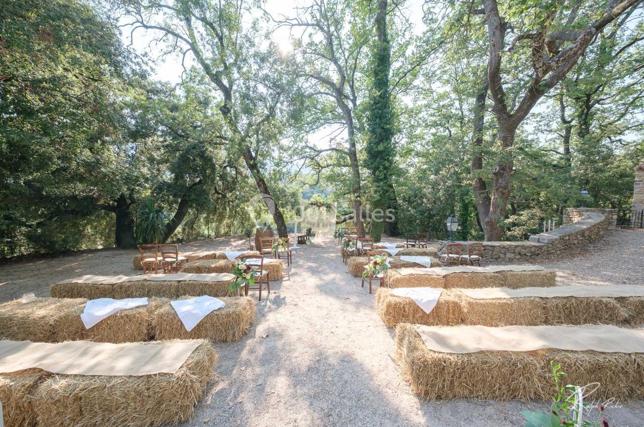 Location salle Signes (Var) - Château de Cancerilles #18 Disposition de bottes de paille et chaises en extérieur sous des arbres, formant un espace pour une cérémonie en plein air.