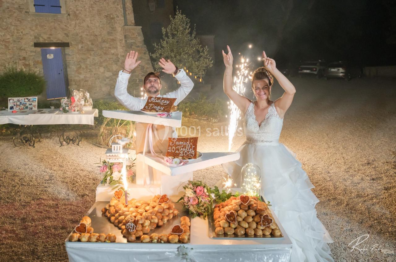 Location salle Signes (Var) - Château de Cancerilles #25 Un couple de mariés souriants célèbre devant une table garnie de desserts et de décorations lumineuses.