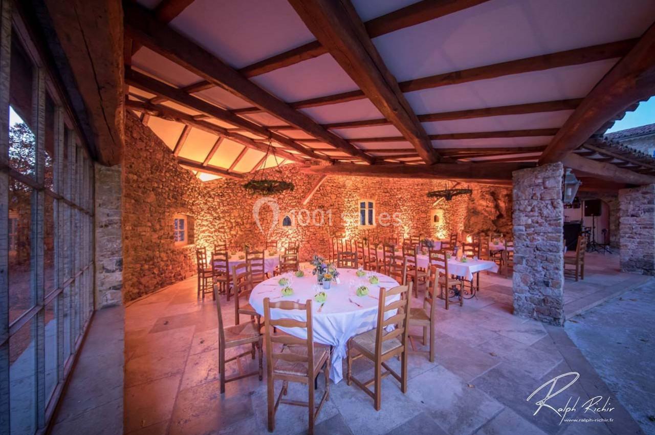 Location salle Signes (Var) - Château de Cancerilles #10 Salle en pierre avec tables rondes dressées, éclairage chaleureux et plafond en poutres apparentes.