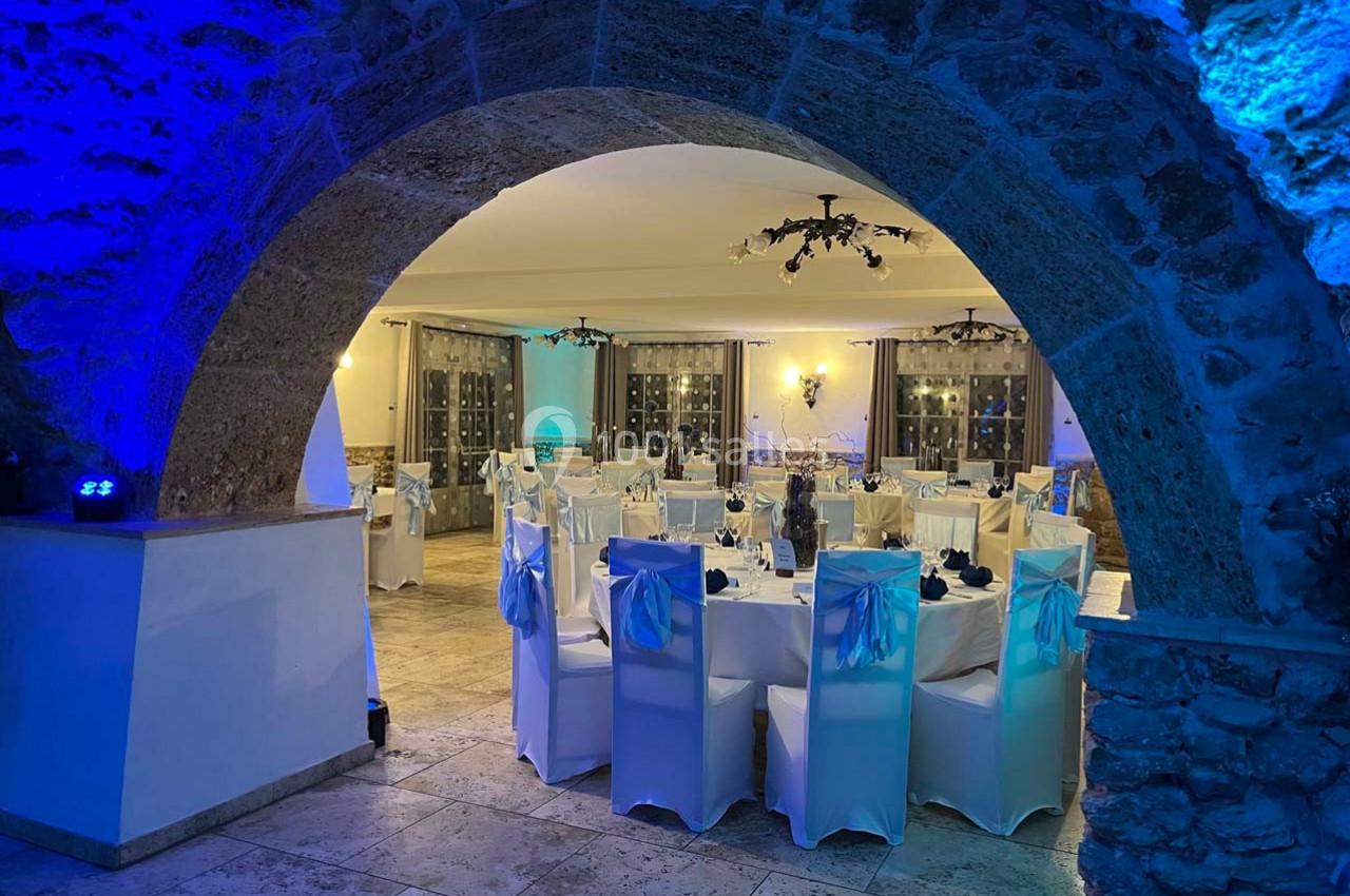 Location salle Signes (Var) - Château de Cancerilles #6 Salle de réception élégamment décorée, avec des tables dressées et des chaises blanches sous un éclairage bleu tamisé.