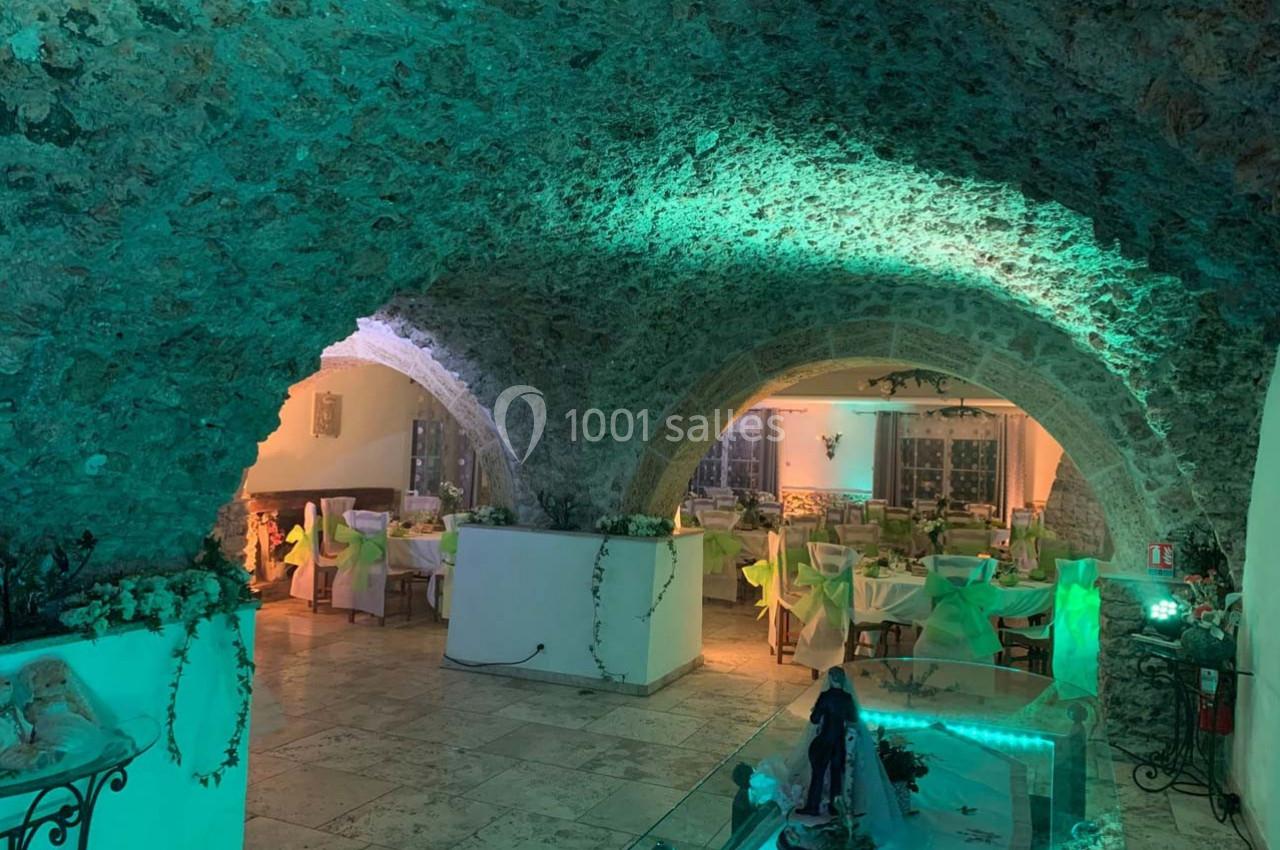 Location salle Signes (Var) - Château de Cancerilles #26 Salle voûtée en pierre avec éclairage vert, tables dressées pour un repas et décoration végétale.