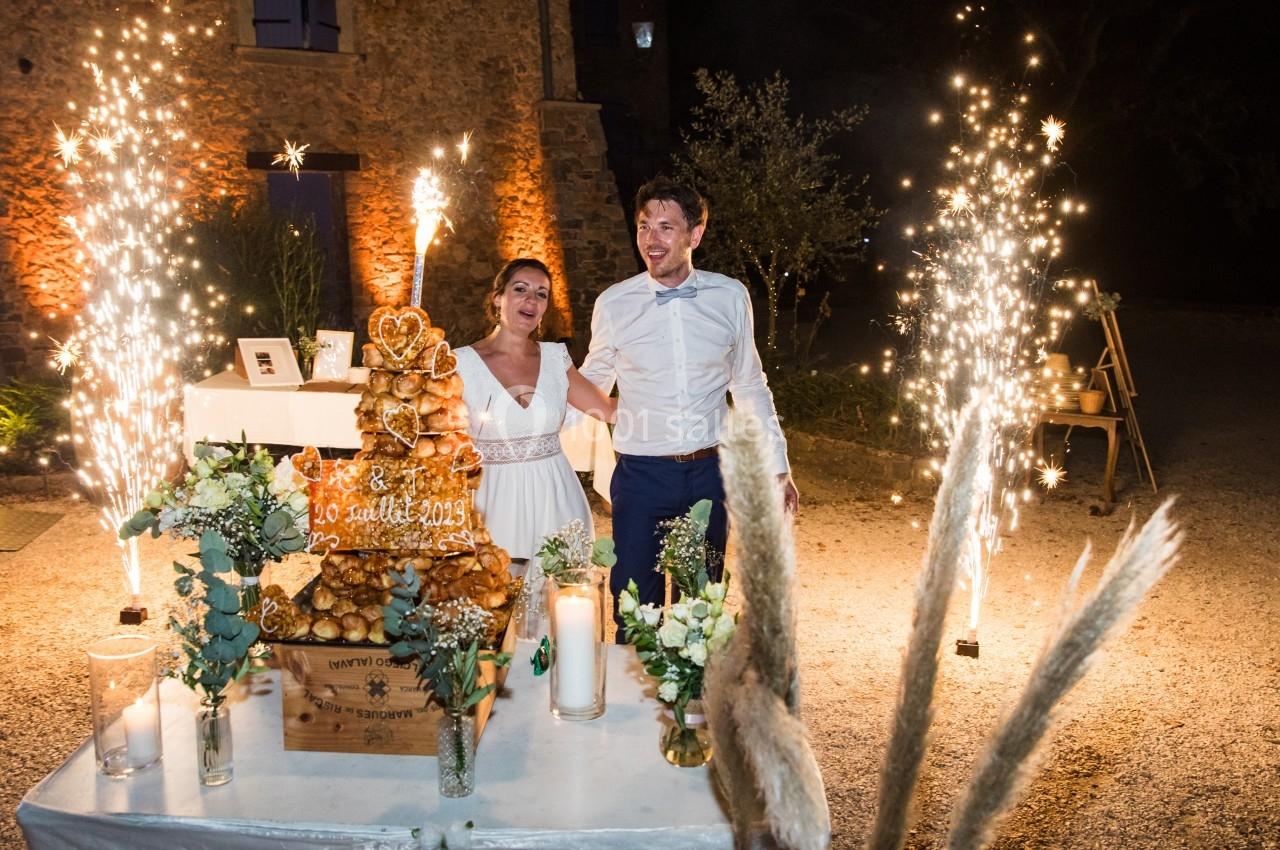 Location salle Signes (Var) - Château de Cancerilles #14 Un couple souriant devant une pièce montée éclairée par des bougies et des feux d'artifice en extérieur, de nuit.