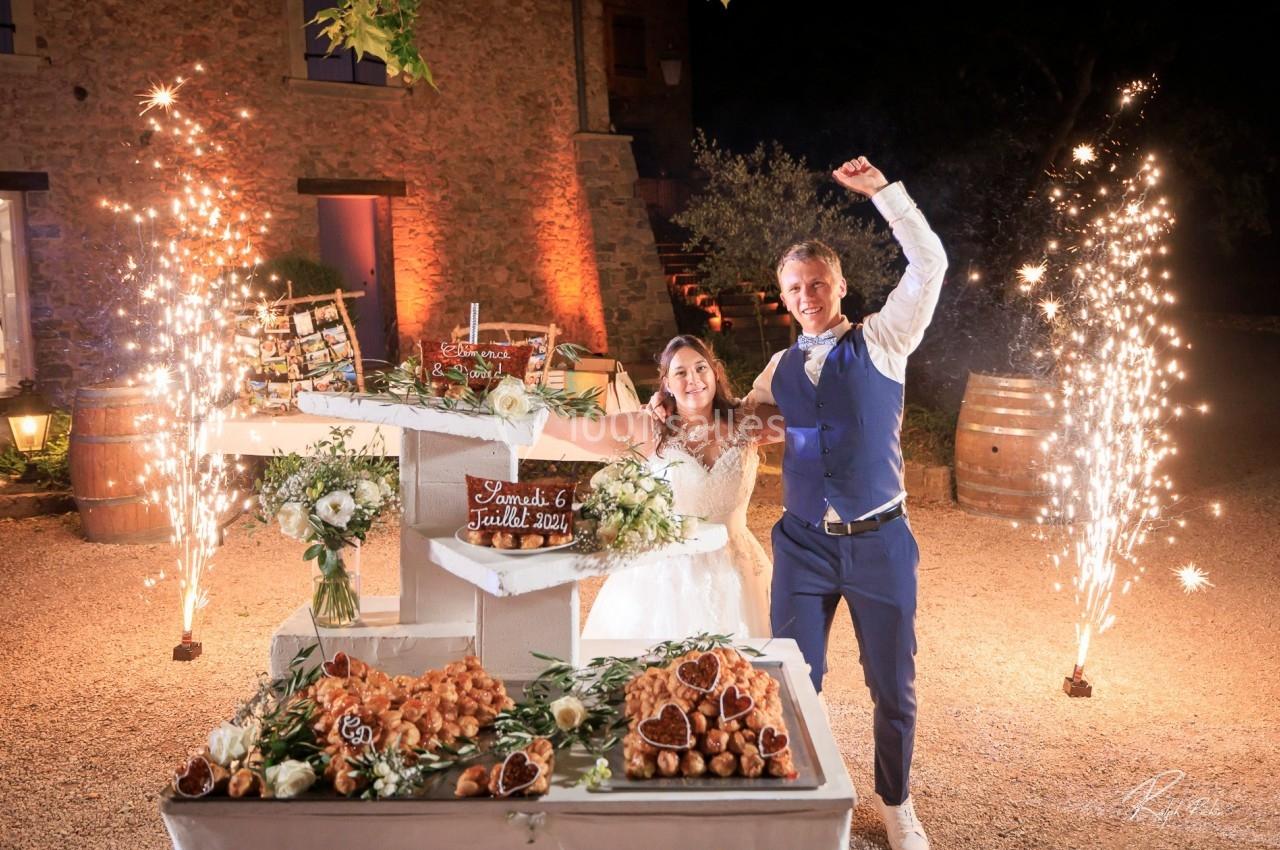Location salle Signes (Var) - Château de Cancerilles #22 Un couple souriant célèbre leur mariage devant une pièce montée décorée, entourée de feux d'artifice.