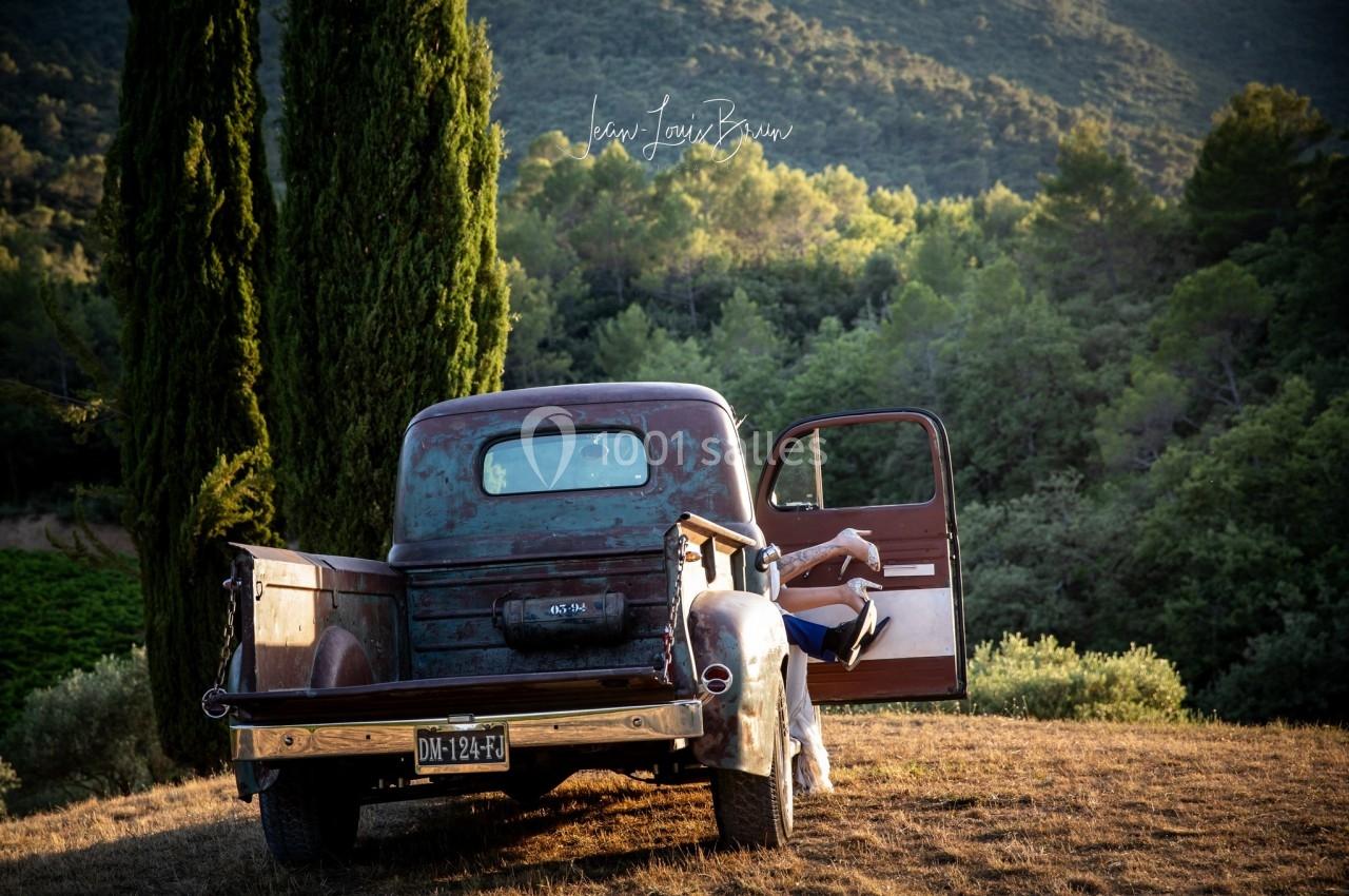Location salle Signes (Var) - Château de Cancerilles #19 Un vieux pick-up rouillé stationné dans un paysage rural avec des collines, des arbres et une personne assise à l'arrière.