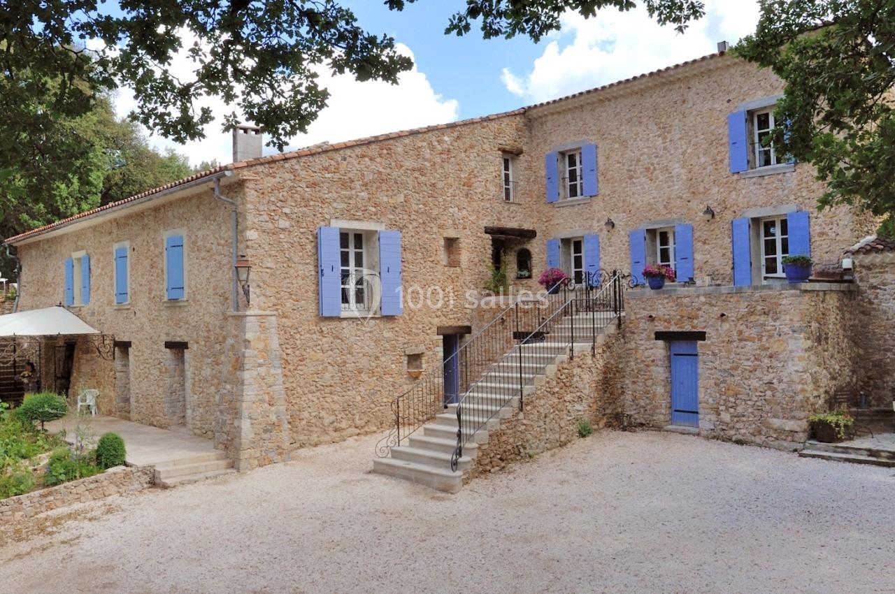 Location salle Signes (Var) - Château de Cancerilles #3 Bâtisse en pierre avec volets bleus, escalier central, cour gravillonnée et arbres en arrière-plan.