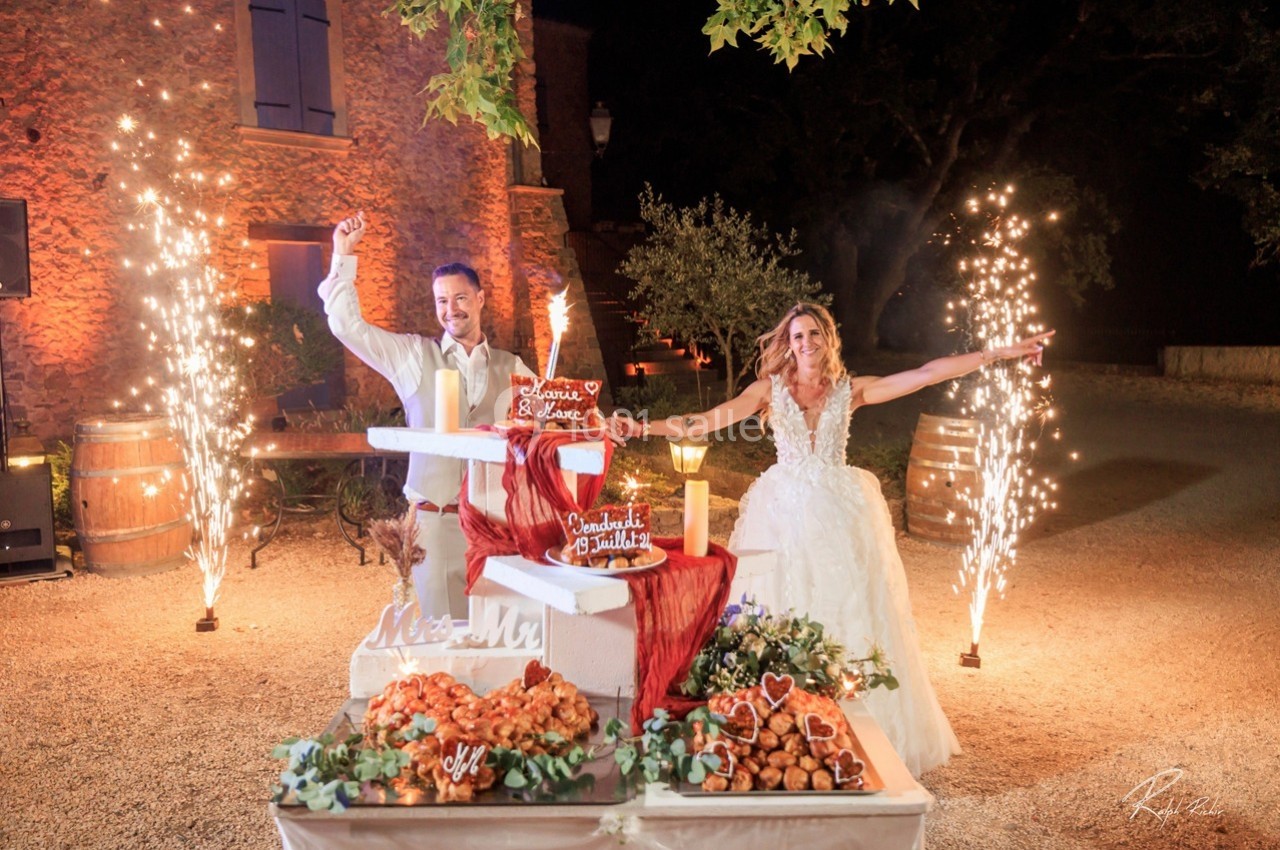 Location salle Signes (Var) - Château de Cancerilles #52 Un couple en tenue de mariage célèbre devant une pièce montée illuminée par des feux d'artifice.
