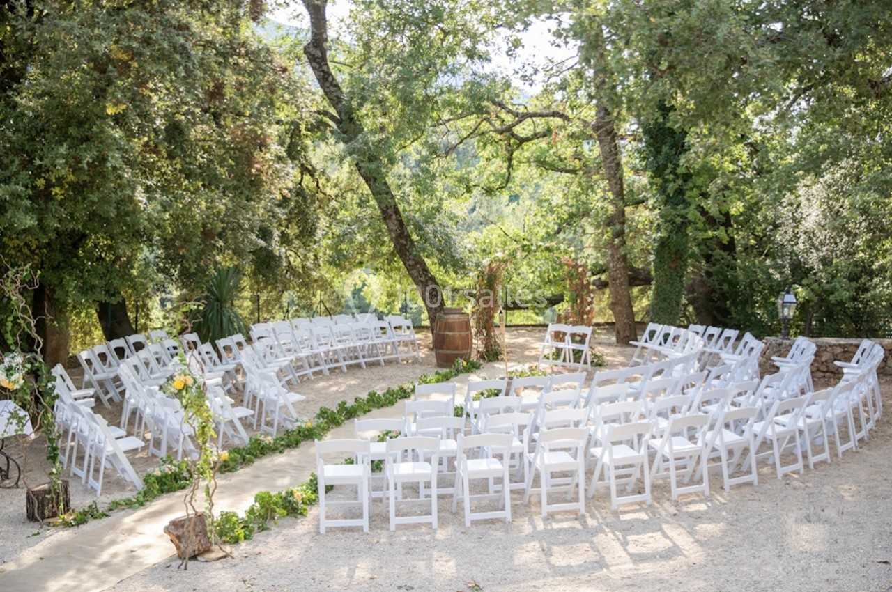 Location salle Signes (Var) - Château de Cancerilles #24 Chaises blanches disposées en cercle dans un cadre extérieur boisé, préparées pour une cérémonie en plein air.