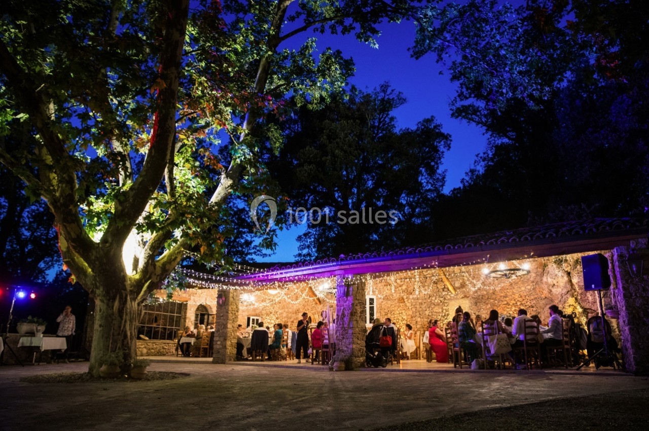 Location salle Signes (Var) - Château de Cancerilles #54 Terrasse éclairée sous un grand arbre, avec des invités assis à des tables lors d'un événement en soirée.