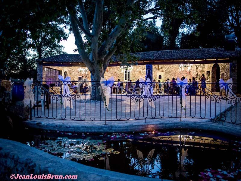 Location salle Signes (Var) - Château de Cancerilles #11 Terrasse éclairée en soirée avec des tables dressées, entourée d'arbres et d'une balustrade près d'un bassin.