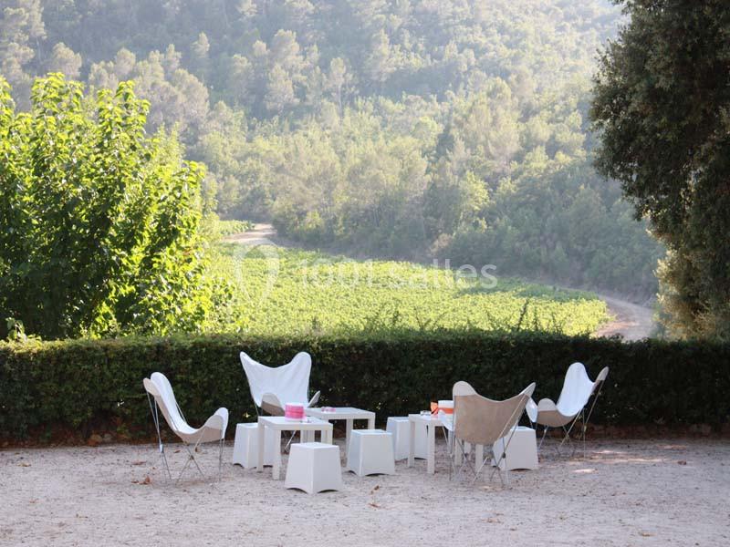 Location salle Signes (Var) - Château de Cancerilles #39 Mobilier de jardin blanc disposé sur une terrasse en gravier, avec vue sur des vignes et une forêt en arrière-plan.