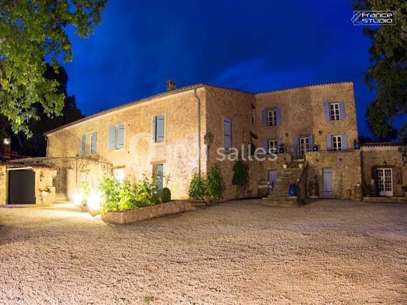 Location salle Signes (Var) - Château de Cancerilles #36 Grande bâtisse en pierre éclairée la nuit, entourée d'une cour en gravier et de végétation.