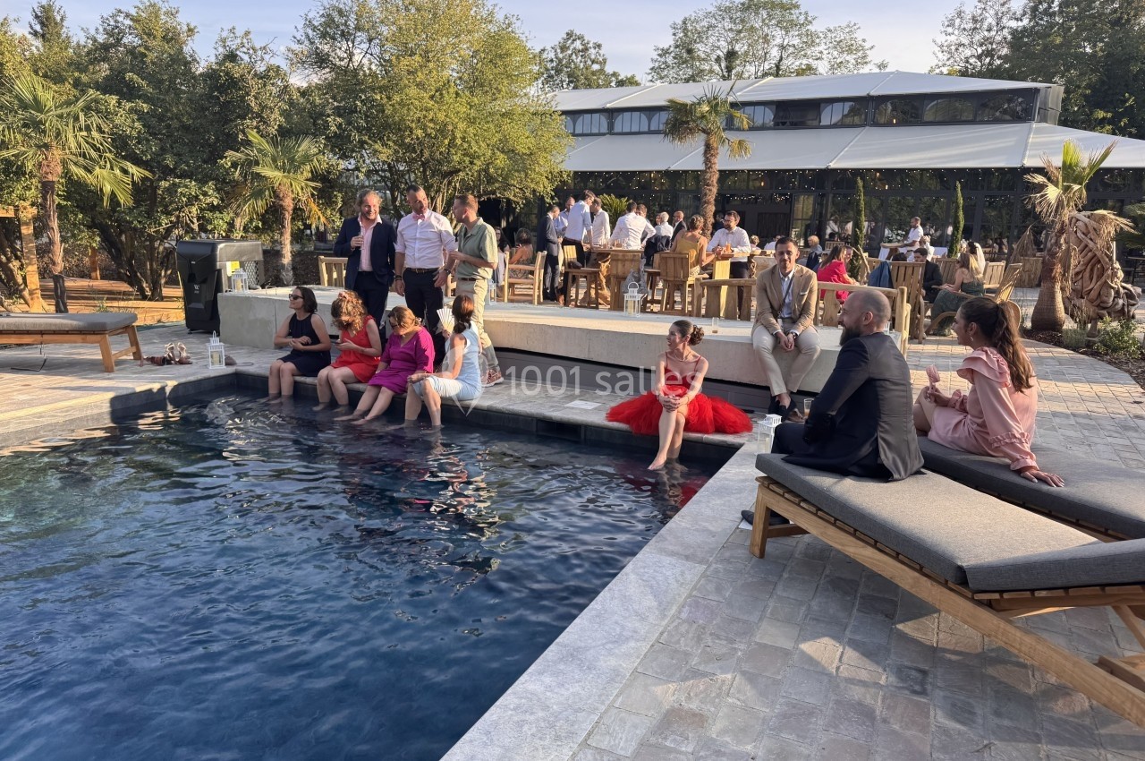 Des personnes assises et debout autour d'une piscine lors d'un événement en extérieur, avec des arbres en arrière-plan.
