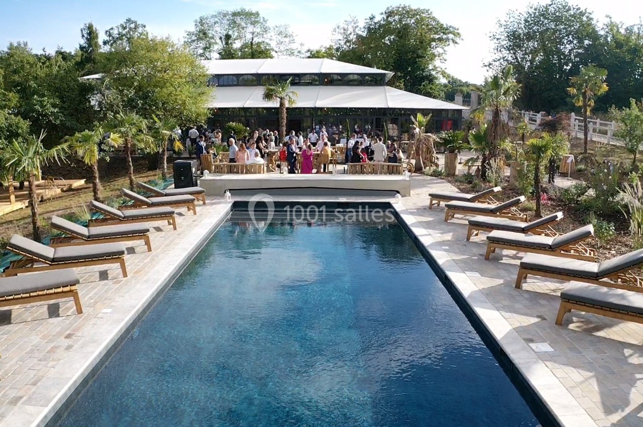 Piscine extérieure entourée de transats, avec un groupe de personnes rassemblées près d'une structure couverte en arrière…