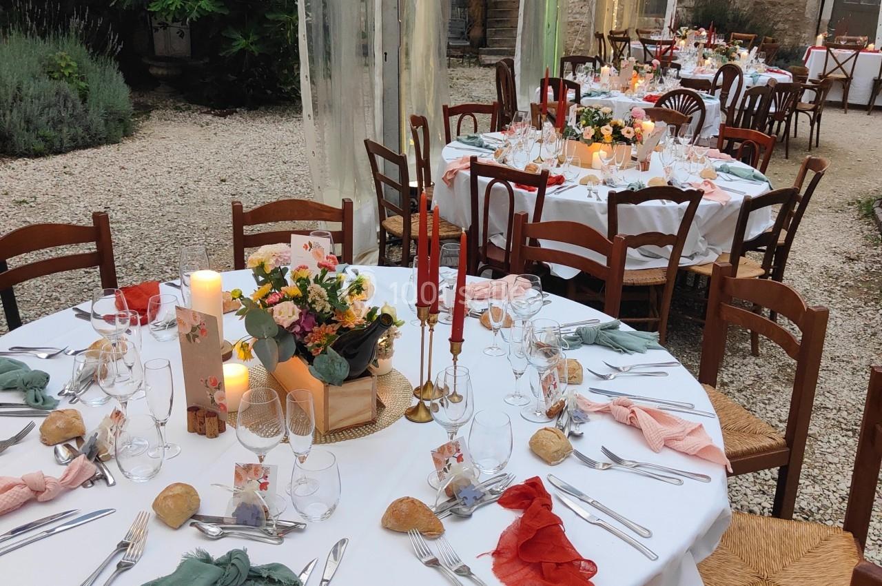 Tables rondes élégamment dressées sous une tente transparente, décorées de bougies, fleurs et serviettes colorées.