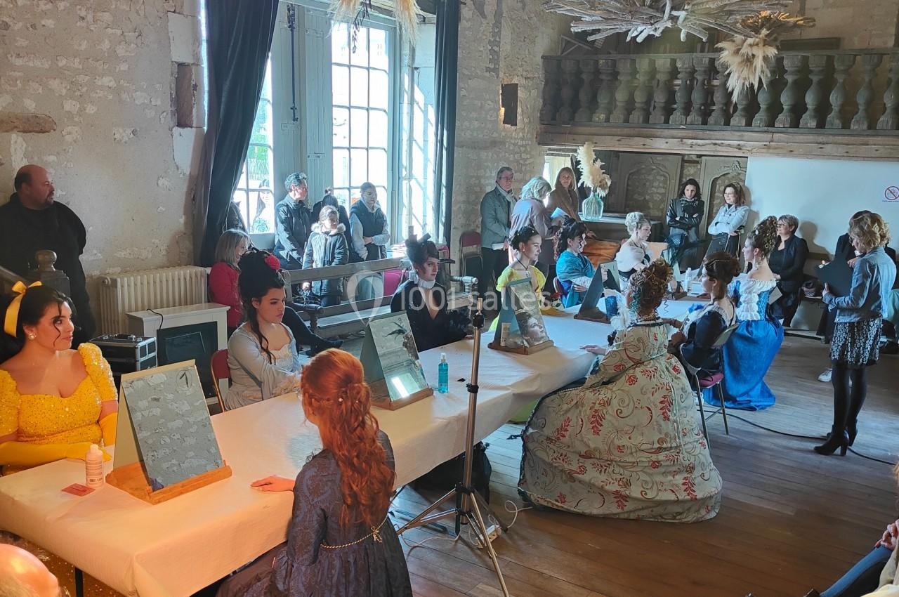 Des personnes en costumes d'époque participent à une activité autour de tables dans une salle au décor ancien.