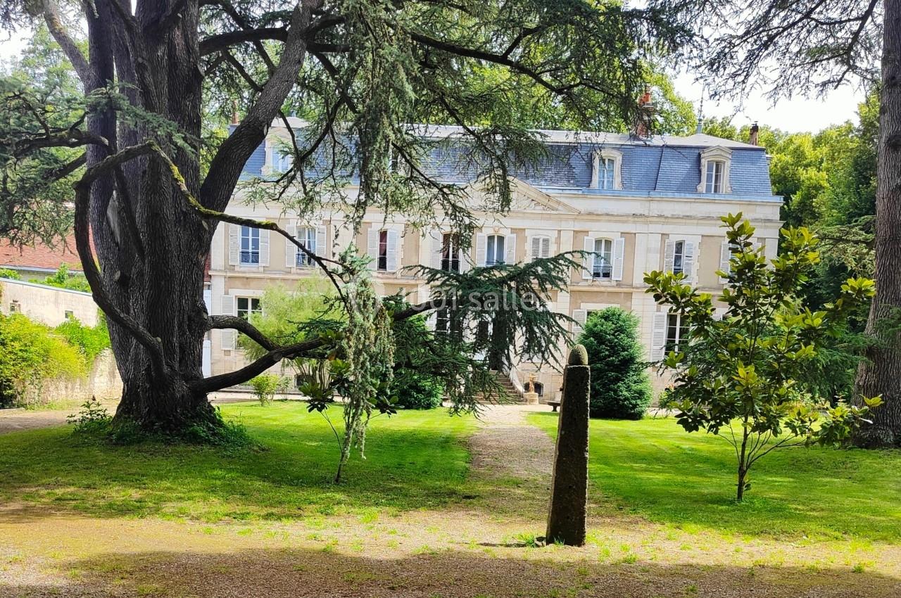 Manoir en pierre blanche entouré d'arbres et de pelouse, avec une allée menant à l'entrée principale.