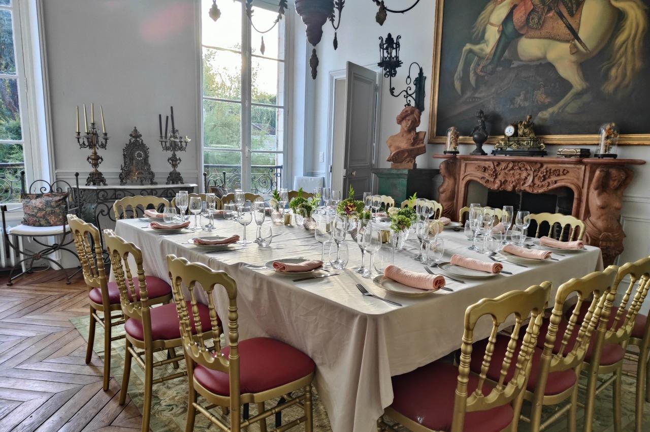 Table élégamment dressée dans une salle décorée de meubles anciens, chandeliers et un grand tableau équestre.