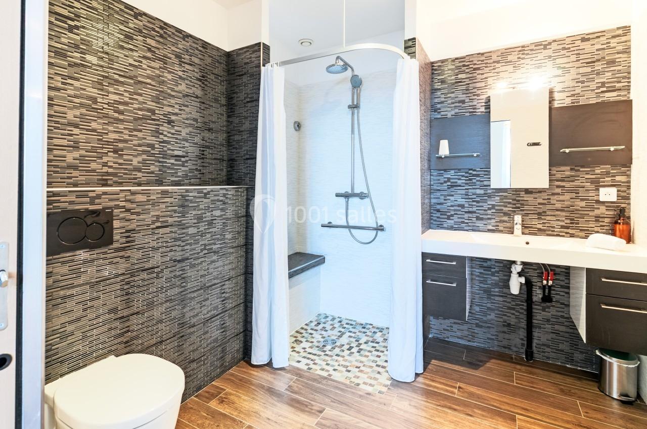 Salle de bain moderne avec douche à l'italienne, carrelage sombre, lavabo suspendu et toilettes.