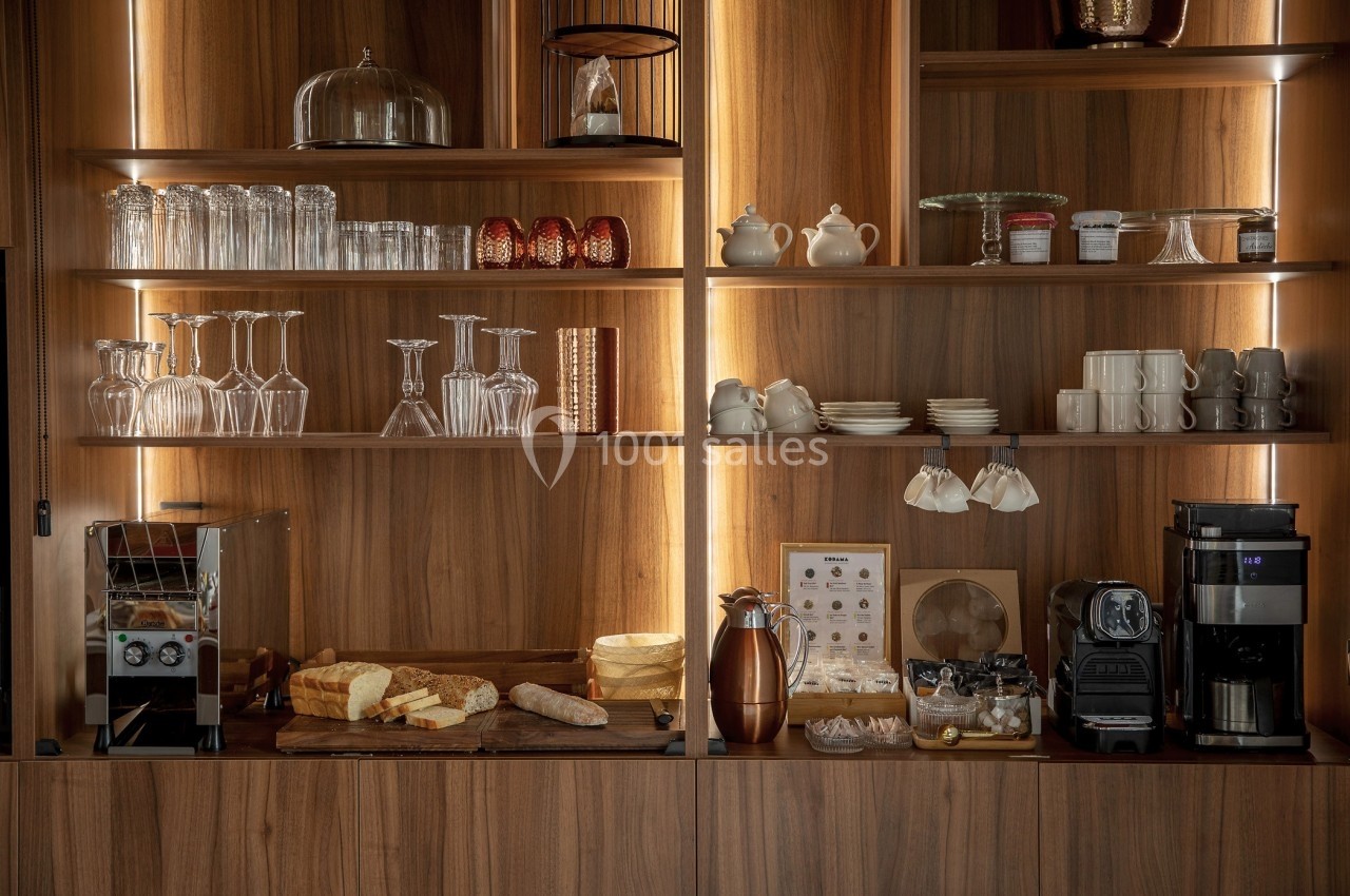 Étagères en bois avec vaisselle, verres, cafetières, machine à café et plateau de fromages et pain.