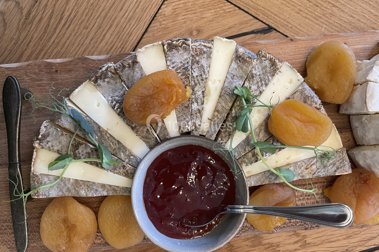 Assiette de fromage avec tranches disposées en éventail, accompagnées d'abricots secs et d'un bol de confiture rouge.
