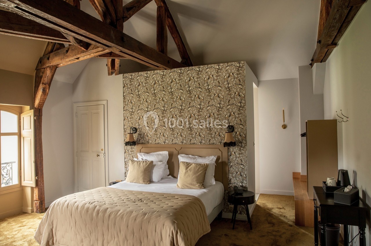 Chambre lumineuse avec poutres apparentes, lit double, tête de lit décorative et mobilier moderne.